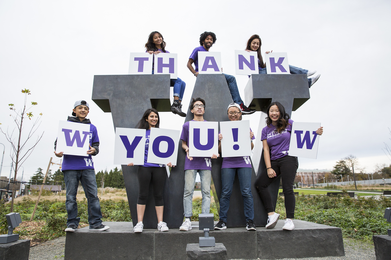 students hold a thank you sign next to the W statue