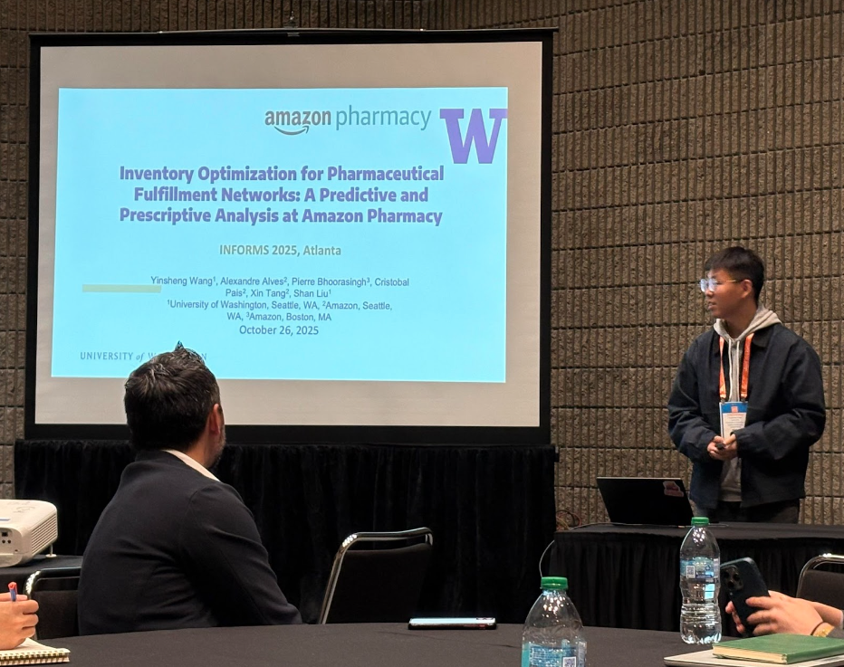 A presenter stands beside a projected slide titled “Inventory Optimization for Pharmaceutical Fulfillment Networks” during an Amazon Pharmacy research talk at an INFORMS conference.