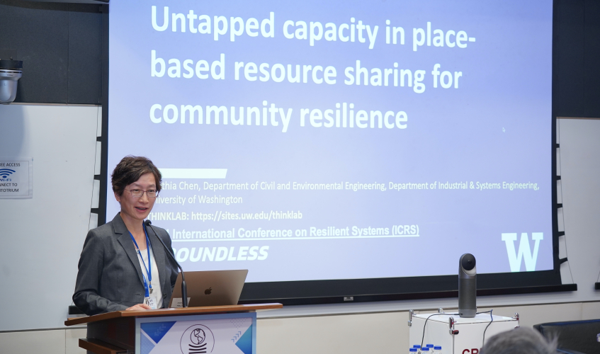 Cynthia Chen presenting her research with a large screen with her title slide behind her