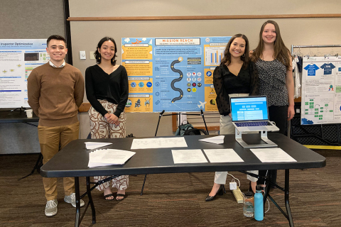 ISE Students stand beside their presentation poster for their Capstone collaboration with All Wheels Up